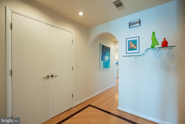 hallway featuring arched walkways, light wood finished floors, recessed lighting, visible vents, and baseboards