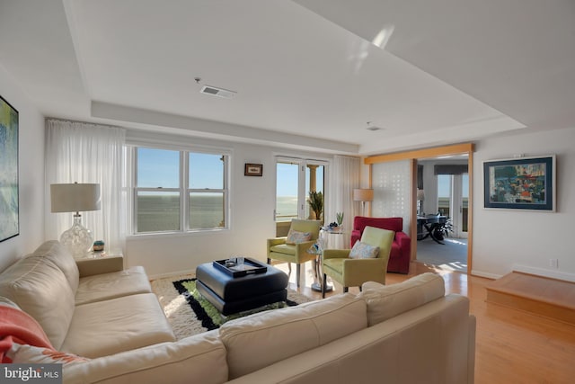 living room with light wood-type flooring, a tray ceiling, visible vents, and baseboards