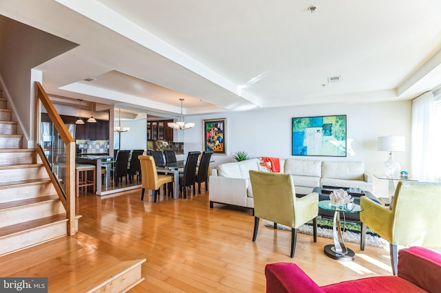 living room featuring stairs, a tray ceiling, wood-type flooring, and a notable chandelier