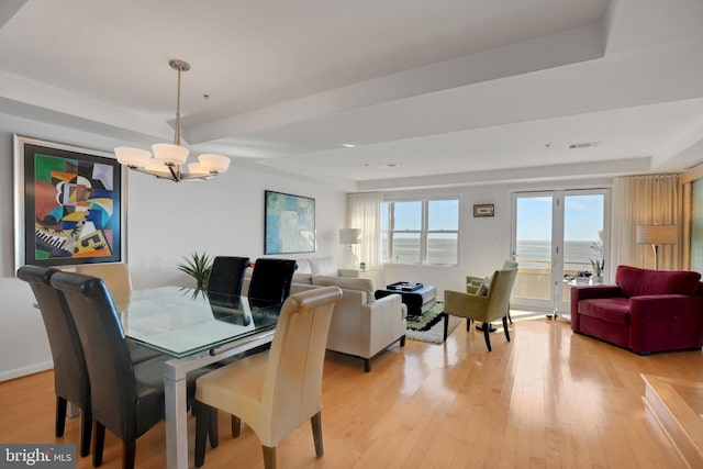 dining area with a tray ceiling, visible vents, light wood finished floors, and an inviting chandelier