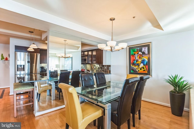 dining area with light wood-type flooring, a raised ceiling, and a notable chandelier