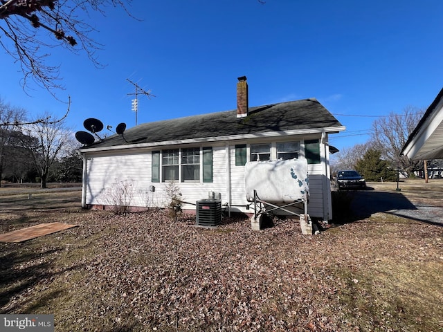 back of house with central AC, a chimney, and roof with shingles