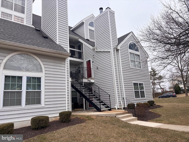 view of property exterior with a shingled roof, a lawn, a chimney, and stairs