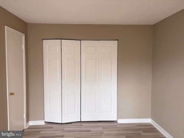 unfurnished bedroom featuring a textured ceiling, a closet, light wood-style flooring, and baseboards