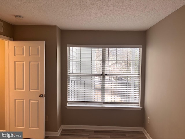 spare room featuring a textured ceiling, baseboards, and wood finished floors