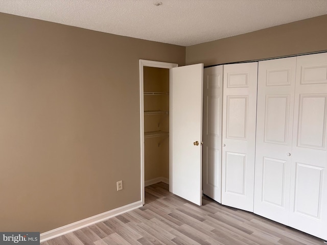 unfurnished bedroom featuring baseboards, a closet, a textured ceiling, and light wood-style floors