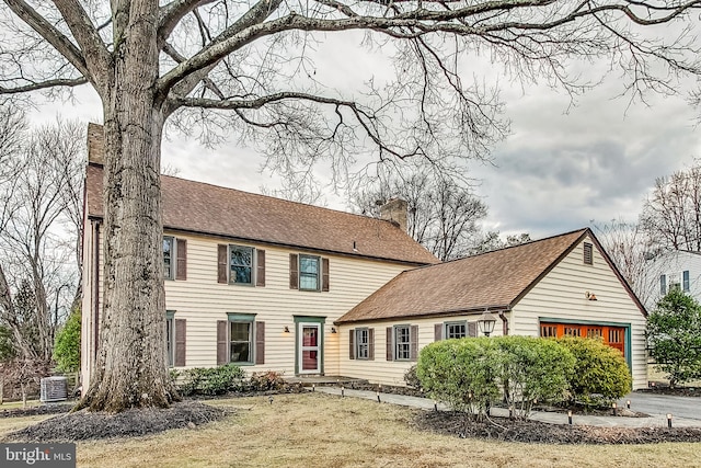 colonial-style house with a garage, a chimney, central AC unit, and roof with shingles