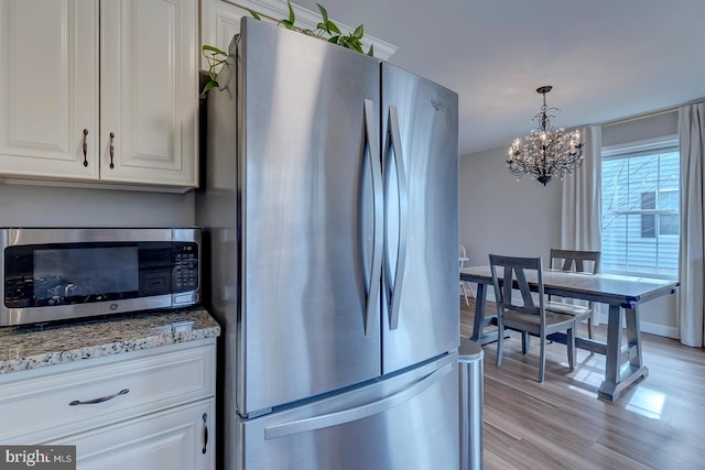 kitchen featuring appliances with stainless steel finishes, white cabinets, light wood-style flooring, and light stone counters