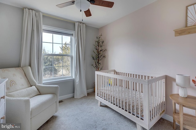 bedroom with a nursery area, baseboards, ceiling fan, and carpet