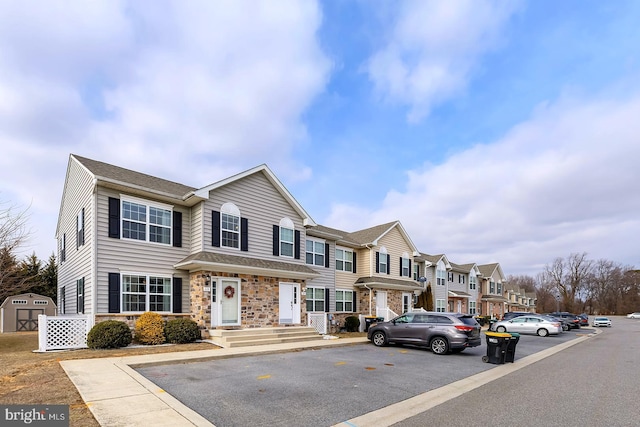 multi unit property featuring a storage shed, stone siding, an outdoor structure, and a residential view