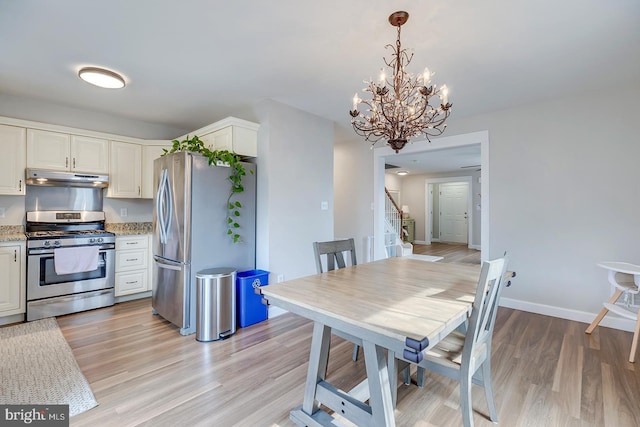 kitchen featuring light stone counters, stainless steel appliances, hanging light fixtures, white cabinets, and under cabinet range hood