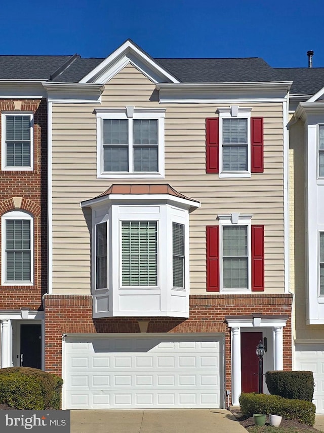 townhome / multi-family property featuring a garage, concrete driveway, brick siding, and roof with shingles