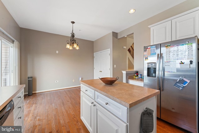 kitchen with light wood-type flooring, stainless steel appliances, white cabinets, and decorative light fixtures