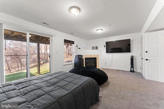 carpeted bedroom featuring a glass covered fireplace, baseboards, and visible vents