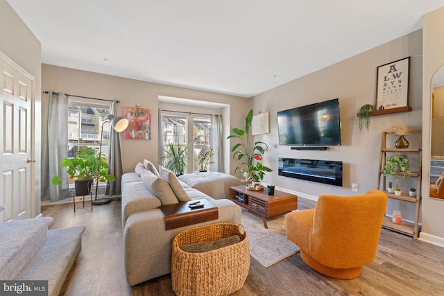 living room with a glass covered fireplace, wood finished floors, and baseboards