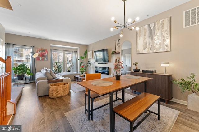 dining space with visible vents, a notable chandelier, wood finished floors, arched walkways, and baseboards