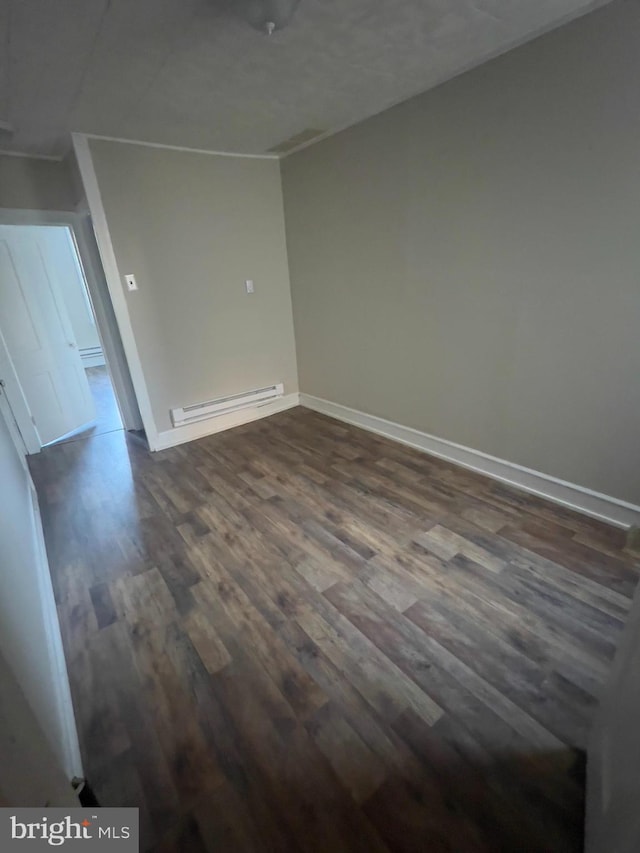 spare room featuring dark wood-type flooring, a baseboard radiator, and baseboards