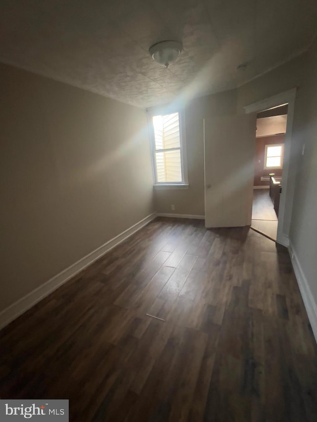 empty room with dark wood-type flooring, a wealth of natural light, and baseboards