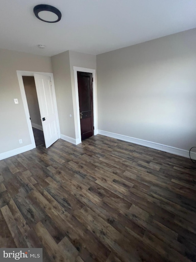 spare room featuring baseboards and dark wood-type flooring