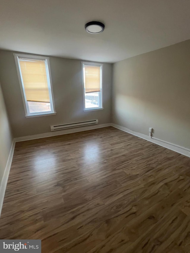 empty room featuring dark wood-style flooring, baseboards, and baseboard heating