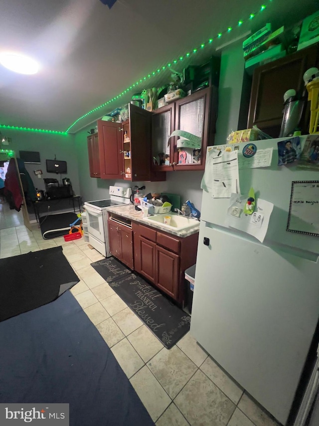 kitchen featuring reddish brown cabinets, light tile patterned floors, light countertops, a sink, and white appliances