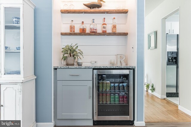 bar with beverage cooler, baseboards, light wood-style flooring, a bar, and stainless steel refrigerator with ice dispenser