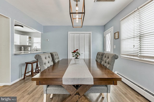 dining area with a baseboard radiator, light wood-style flooring, and baseboards