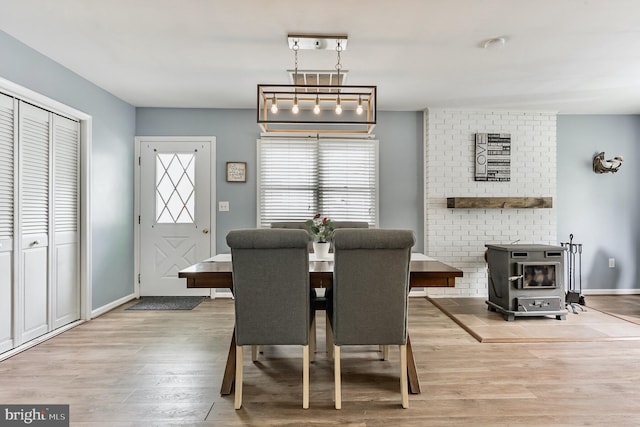 dining space with light wood finished floors, a wood stove, and baseboards