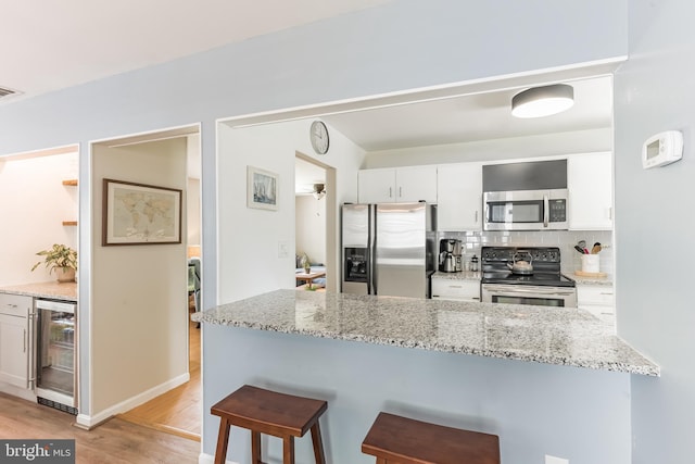 kitchen featuring beverage cooler, white cabinets, appliances with stainless steel finishes, a kitchen breakfast bar, and light wood-type flooring