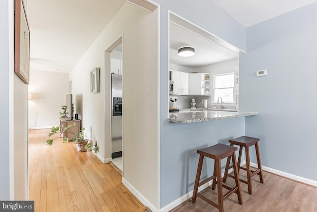 corridor featuring light wood-style flooring, baseboards, and a sink