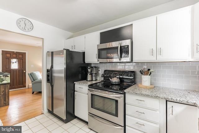 kitchen featuring stainless steel appliances, tasteful backsplash, white cabinetry, and light stone countertops