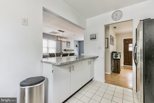 kitchen featuring light tile patterned floors, visible vents, decorative light fixtures, freestanding refrigerator, and white cabinetry