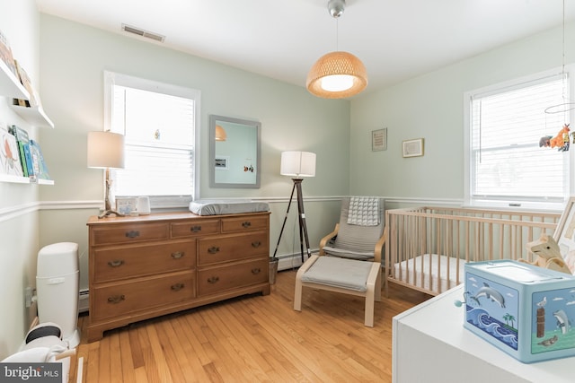 bedroom with a baseboard radiator, visible vents, light wood-style flooring, and multiple windows