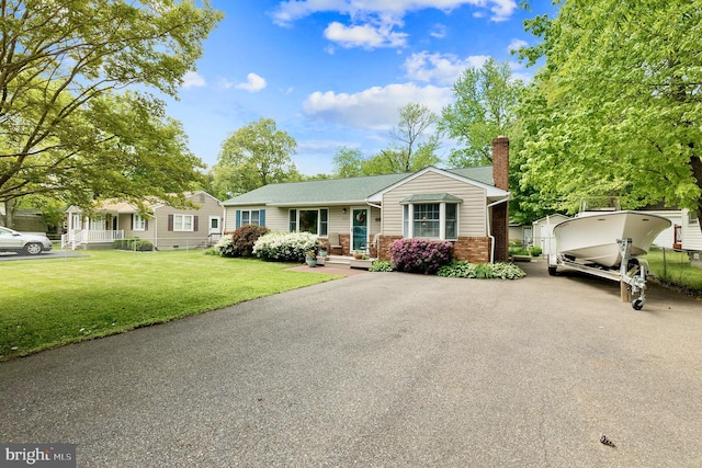 view of front of home with aphalt driveway, a chimney, a front lawn, and brick siding