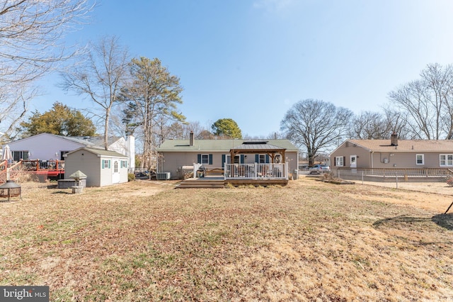 rear view of property with fence, a deck, an outdoor structure, and a lawn