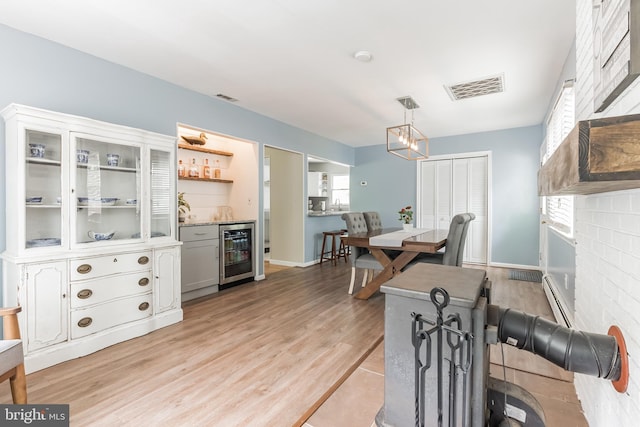 dining room with a dry bar, visible vents, wine cooler, light wood-type flooring, and a baseboard heating unit