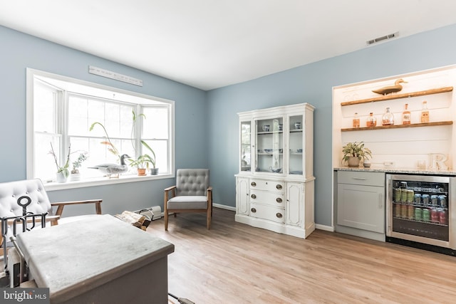 office space with a dry bar, visible vents, a baseboard radiator, wine cooler, and light wood-style floors