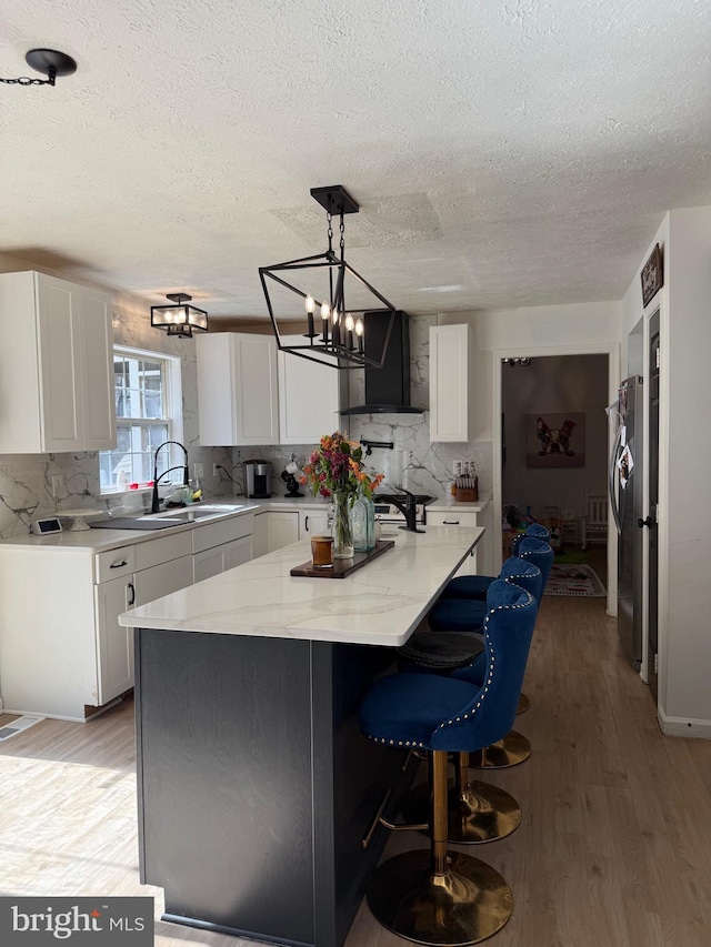 kitchen featuring white cabinetry, a sink, light wood-style flooring, and wall chimney exhaust hood