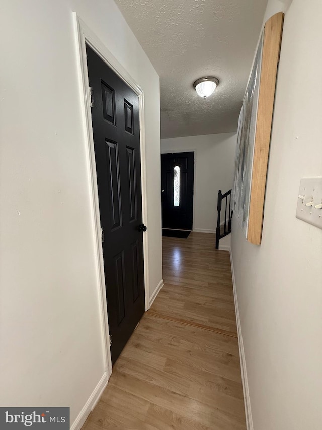 hall featuring a textured ceiling, light wood finished floors, stairs, and baseboards