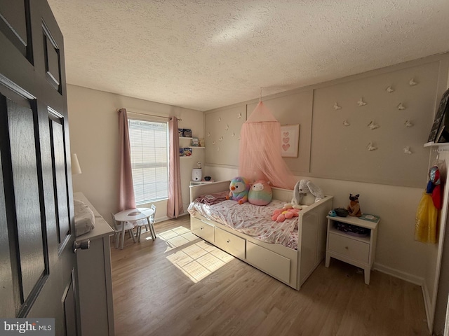 bedroom with light wood-style floors, baseboards, and a textured ceiling