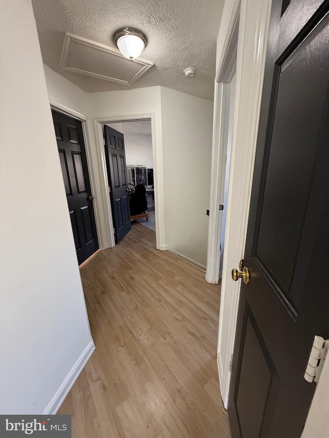 hall with attic access, baseboards, a textured ceiling, and light wood finished floors