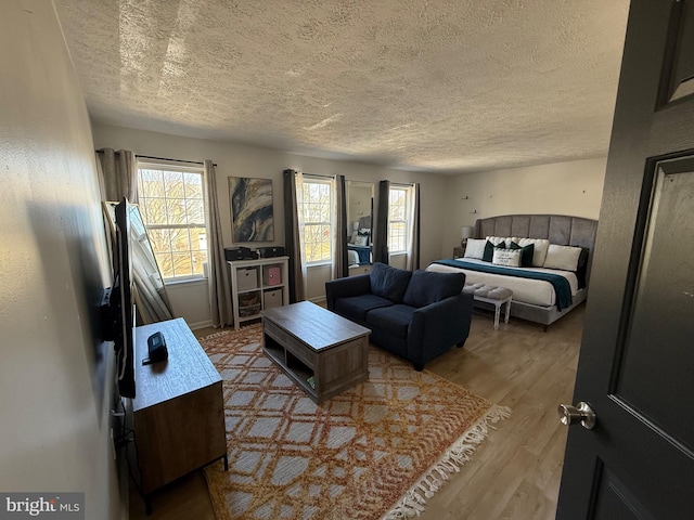 bedroom featuring multiple windows, a textured ceiling, baseboards, and wood finished floors