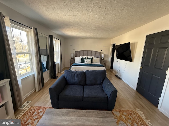 bedroom featuring light wood-style floors, visible vents, a textured ceiling, and baseboards