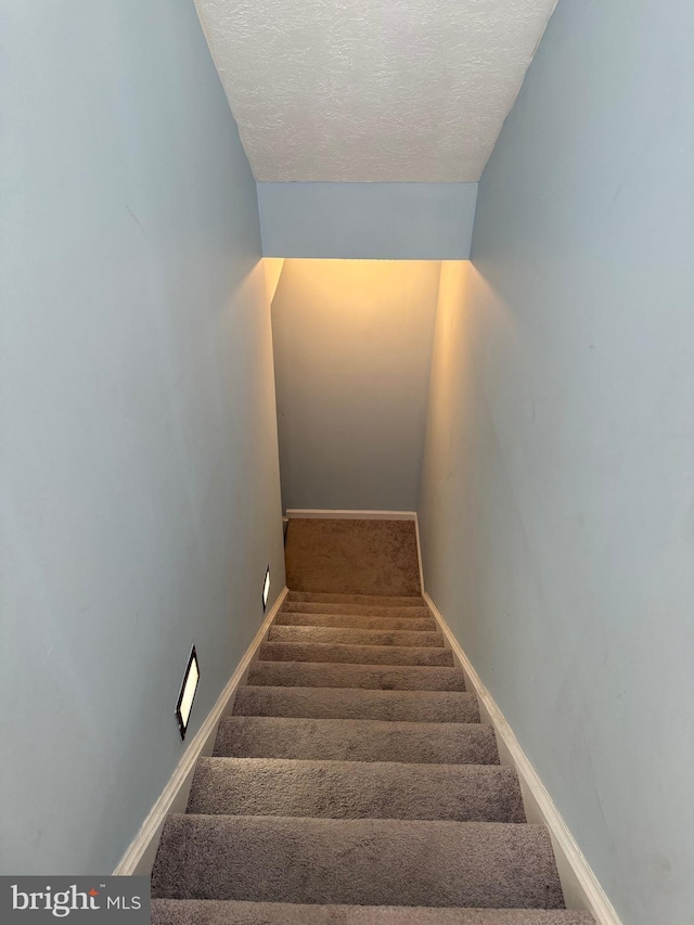 stairway featuring carpet flooring, a textured ceiling, and baseboards