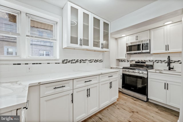 kitchen featuring stainless steel appliances, light wood-style floors, glass insert cabinets, white cabinets, and light stone countertops