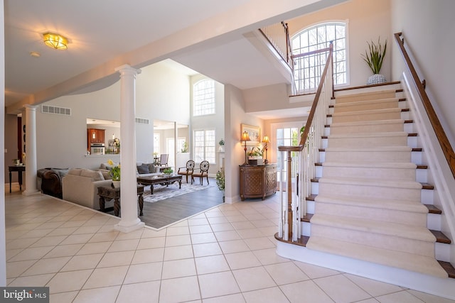 entryway featuring light tile patterned floors, decorative columns, visible vents, stairway, and high vaulted ceiling