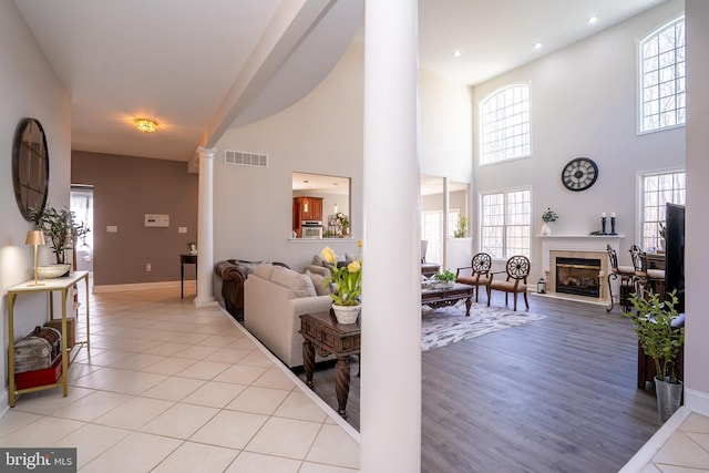 living room with light tile patterned floors, visible vents, baseboards, a glass covered fireplace, and decorative columns