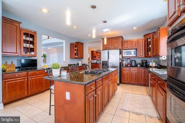 kitchen featuring light tile patterned floors, a kitchen island, glass insert cabinets, appliances with stainless steel finishes, and a breakfast bar area