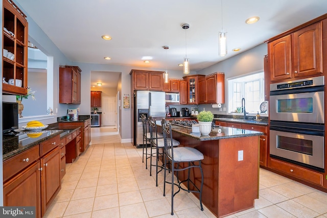 kitchen with light tile patterned floors, a breakfast bar area, stainless steel appliances, dark stone countertops, and glass insert cabinets