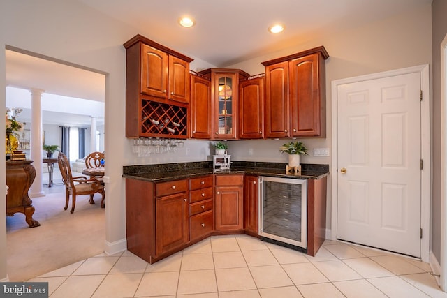 kitchen with wine cooler, recessed lighting, decorative columns, dark stone countertops, and glass insert cabinets